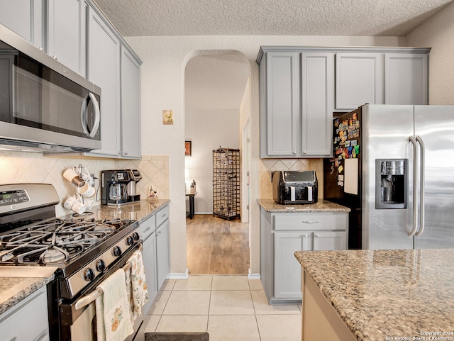 kitchen with a textured ceiling, stainless steel appliances, light stone counters, and light tile patterned flooring