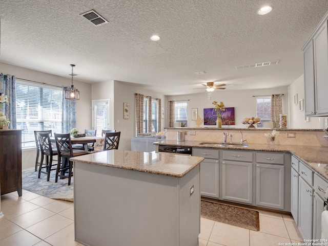 kitchen with a center island, light stone counters, a textured ceiling, decorative light fixtures, and light tile patterned floors