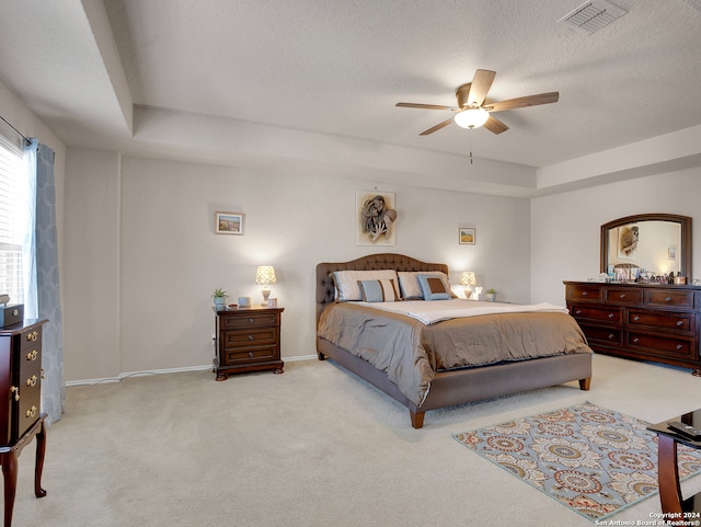 carpeted bedroom with a textured ceiling, a tray ceiling, and ceiling fan