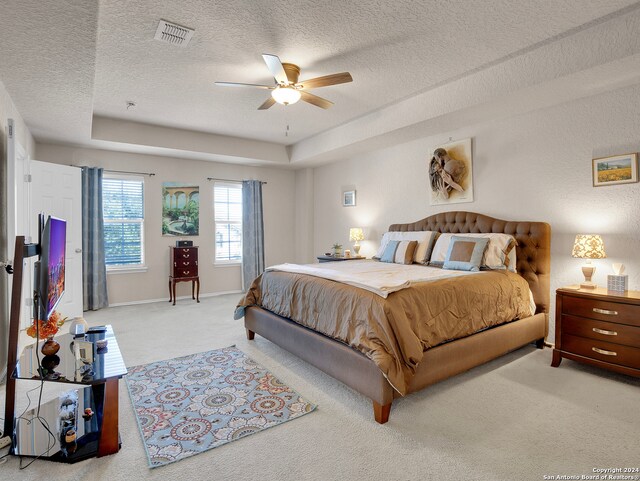 carpeted bedroom with ceiling fan, a raised ceiling, and a textured ceiling