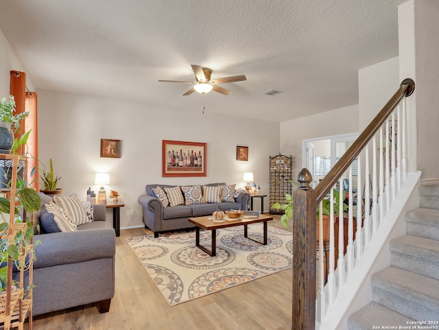 living room with ceiling fan, a textured ceiling, and light wood-type flooring