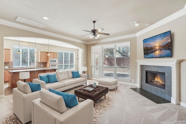 living room with crown molding, a fireplace, ceiling fan, and light colored carpet