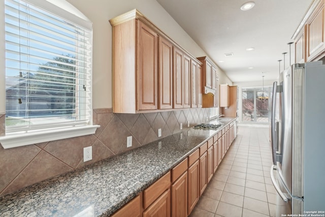 kitchen with dark stone counters, hanging light fixtures, light tile patterned floors, tasteful backsplash, and stainless steel appliances