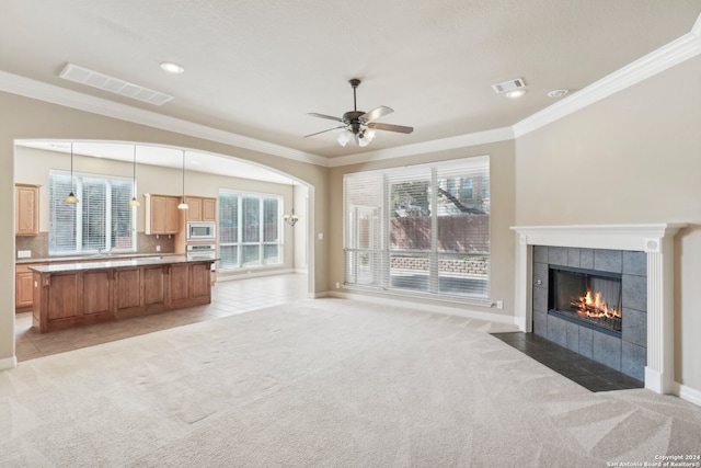 unfurnished living room featuring a fireplace, light colored carpet, a wealth of natural light, and crown molding