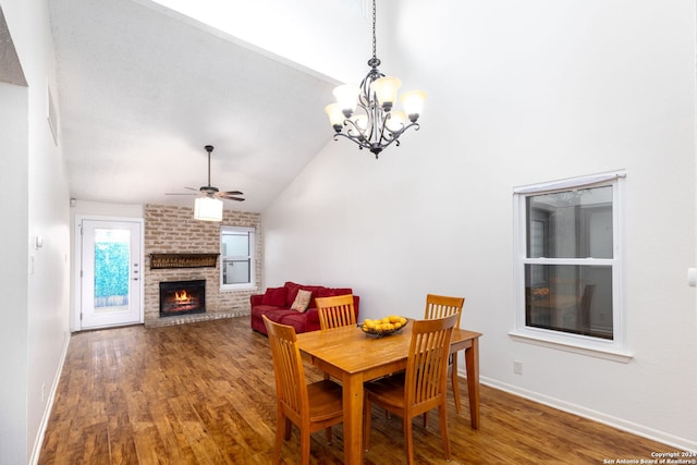 dining space featuring ceiling fan with notable chandelier, hardwood / wood-style floors, vaulted ceiling, and a brick fireplace