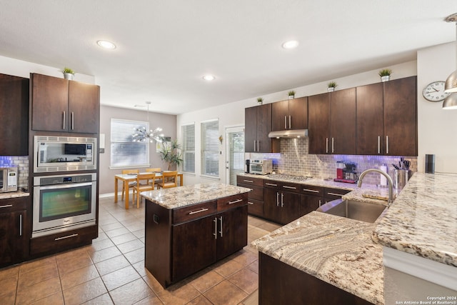 kitchen featuring sink, light stone counters, backsplash, a kitchen island, and appliances with stainless steel finishes