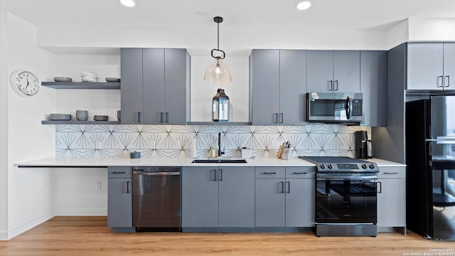 kitchen featuring backsplash, light hardwood / wood-style flooring, hanging light fixtures, and appliances with stainless steel finishes