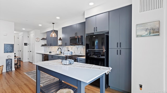 kitchen with decorative backsplash, sink, black appliances, light hardwood / wood-style floors, and hanging light fixtures