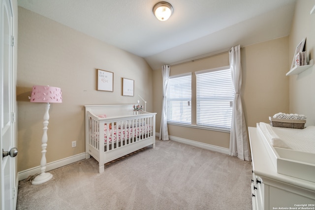 bedroom featuring light colored carpet, lofted ceiling, and a nursery area