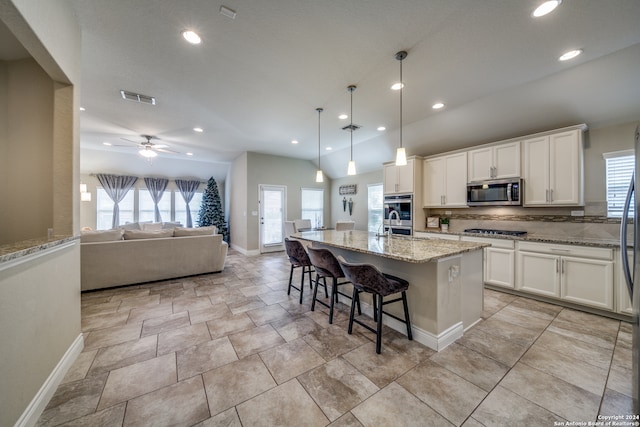 kitchen with a wealth of natural light, a center island with sink, ceiling fan, and appliances with stainless steel finishes