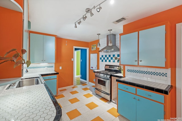 kitchen with backsplash, tile counters, wall chimney range hood, and stainless steel gas range