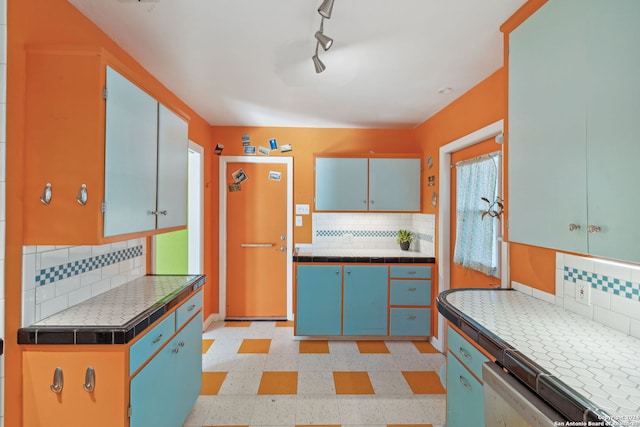 kitchen featuring dishwasher, backsplash, rail lighting, and tile counters