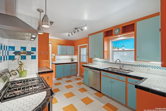 kitchen featuring tile counters, wall chimney exhaust hood, stainless steel appliances, sink, and pendant lighting