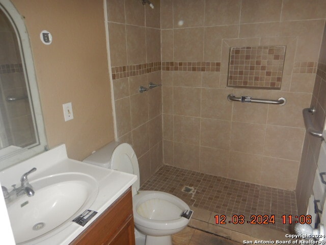 bathroom with tiled shower, tile patterned flooring, vanity, and toilet