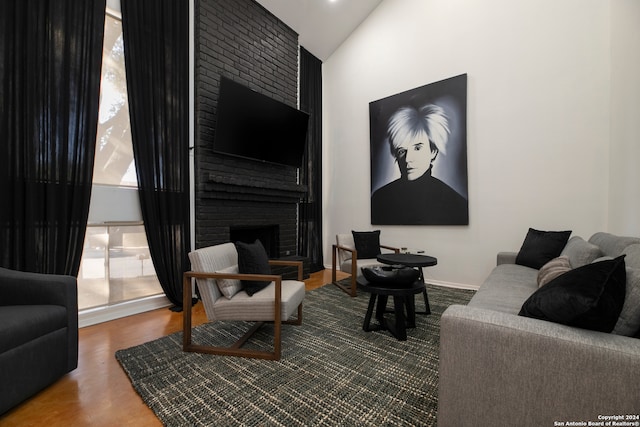 living room featuring wood-type flooring, vaulted ceiling, and a brick fireplace