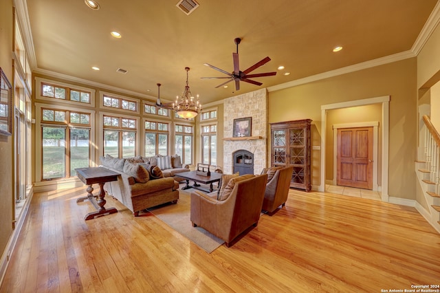 living room featuring ceiling fan with notable chandelier, light hardwood / wood-style floors, a stone fireplace, and ornamental molding