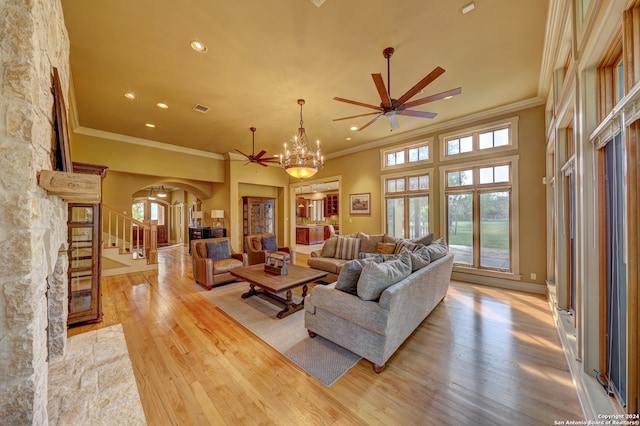 living room with ceiling fan with notable chandelier, light hardwood / wood-style floors, ornamental molding, and a towering ceiling