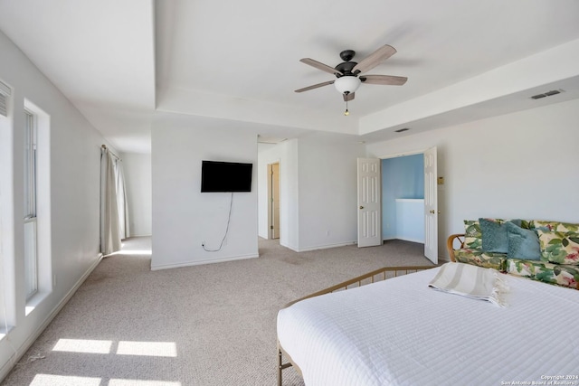 bedroom featuring ceiling fan, light colored carpet, and a tray ceiling