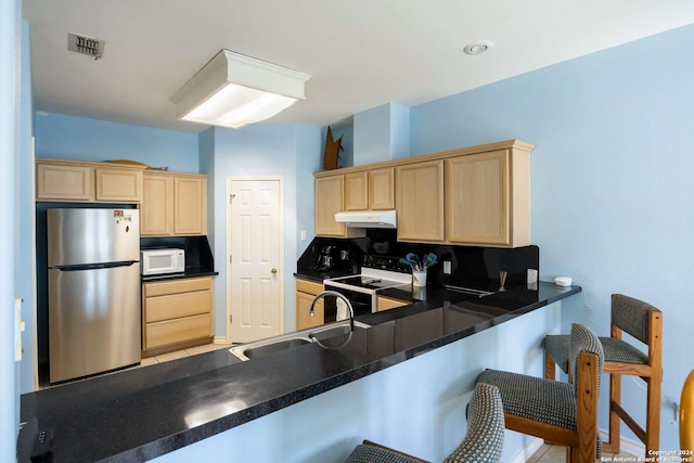 kitchen with white appliances, a kitchen breakfast bar, sink, light brown cabinetry, and kitchen peninsula