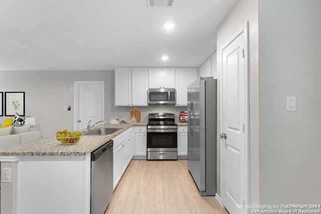 kitchen with sink, stainless steel appliances, light stone counters, white cabinets, and light wood-type flooring