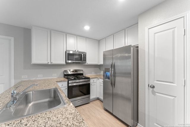 kitchen featuring light stone countertops, appliances with stainless steel finishes, sink, white cabinets, and light hardwood / wood-style floors