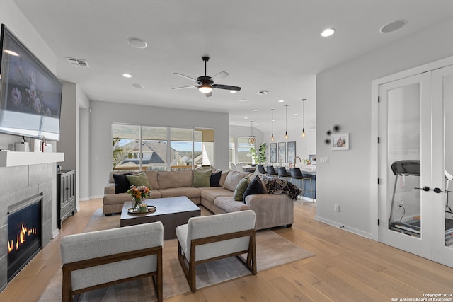 living room with ceiling fan, light wood-type flooring, and a tiled fireplace