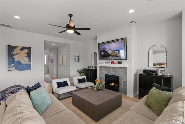 living room with a tiled fireplace, ceiling fan, and light wood-type flooring