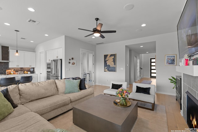 living room with a tiled fireplace, ceiling fan, and light hardwood / wood-style flooring