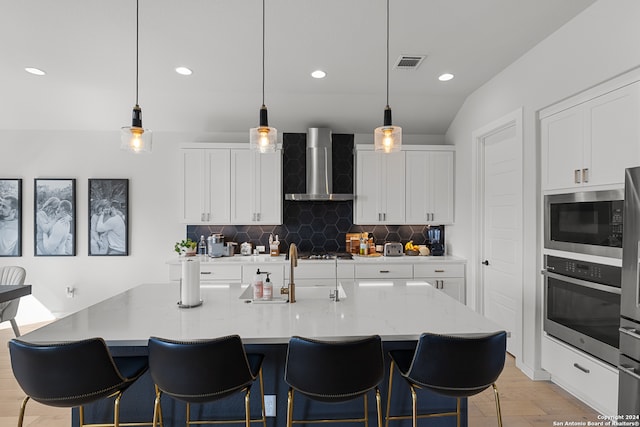 kitchen featuring white cabinetry, wall chimney range hood, appliances with stainless steel finishes, and light hardwood / wood-style flooring