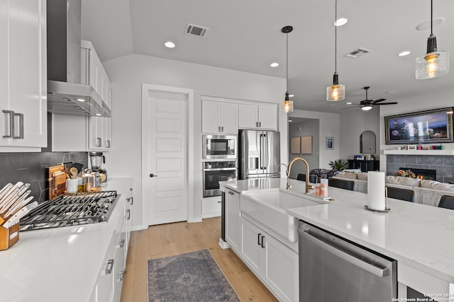 kitchen with stainless steel appliances, ceiling fan, pendant lighting, white cabinetry, and a tiled fireplace