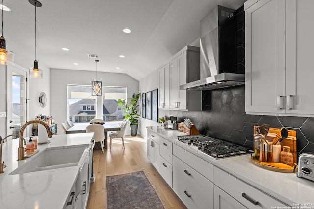 kitchen with sink, wall chimney range hood, white cabinets, light hardwood / wood-style floors, and lofted ceiling