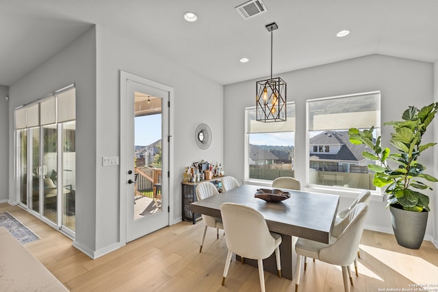 dining area with light wood-type flooring, vaulted ceiling, plenty of natural light, and a notable chandelier