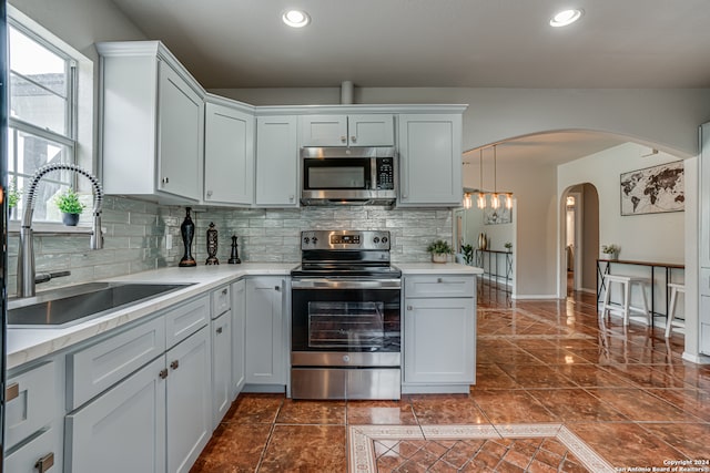 kitchen featuring sink, pendant lighting, decorative backsplash, dark tile patterned flooring, and appliances with stainless steel finishes