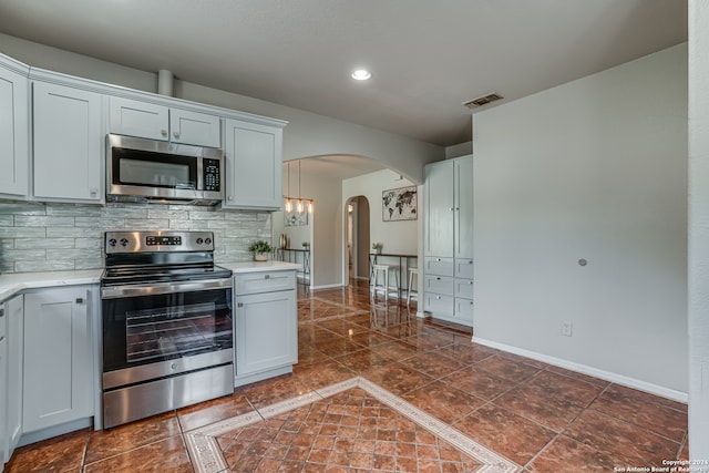 kitchen featuring white cabinets, appliances with stainless steel finishes, decorative backsplash, and pendant lighting