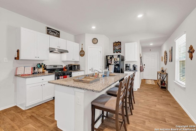 kitchen with stainless steel appliances, a kitchen breakfast bar, a kitchen island with sink, white cabinets, and light wood-type flooring