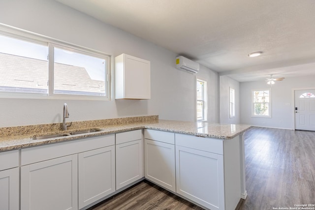 kitchen with light stone countertops, white cabinetry, dark wood-type flooring, and a wall mounted air conditioner