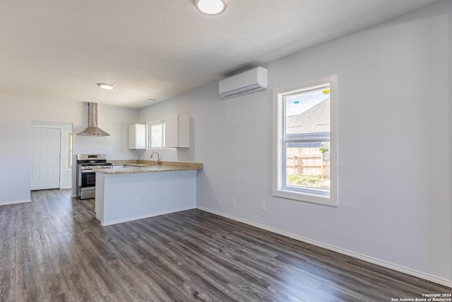 kitchen with wall chimney exhaust hood, stainless steel range oven, a wall unit AC, kitchen peninsula, and white cabinets