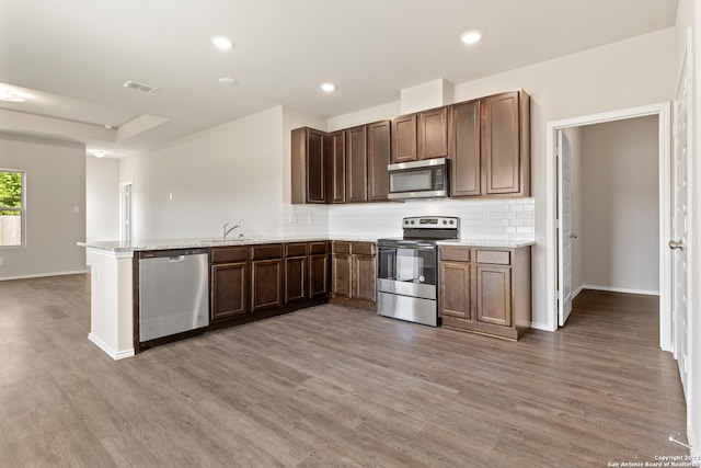 kitchen featuring hardwood / wood-style flooring, decorative backsplash, kitchen peninsula, and stainless steel appliances