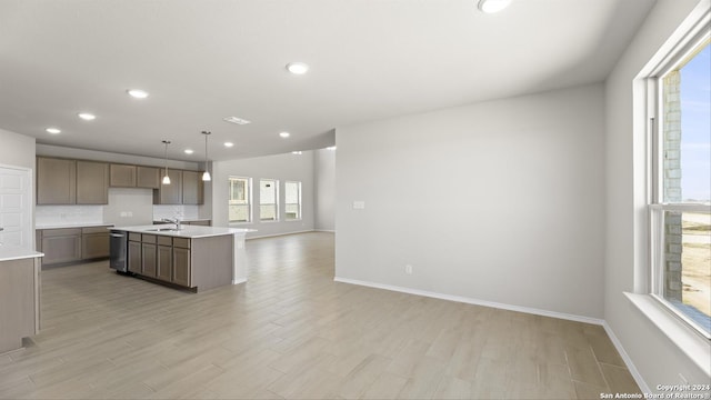 kitchen featuring a center island with sink, stainless steel dishwasher, light wood-type flooring, and hanging light fixtures