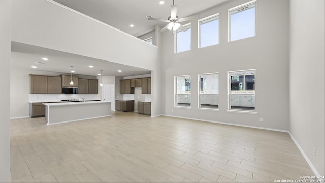 unfurnished living room featuring ceiling fan, light hardwood / wood-style floors, and a high ceiling