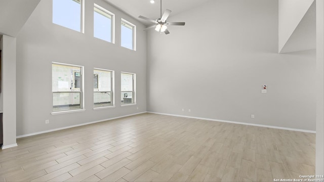 unfurnished living room with a towering ceiling, light wood-type flooring, plenty of natural light, and ceiling fan