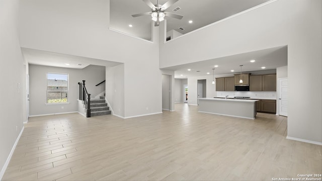 unfurnished living room with ceiling fan, light wood-type flooring, and a high ceiling