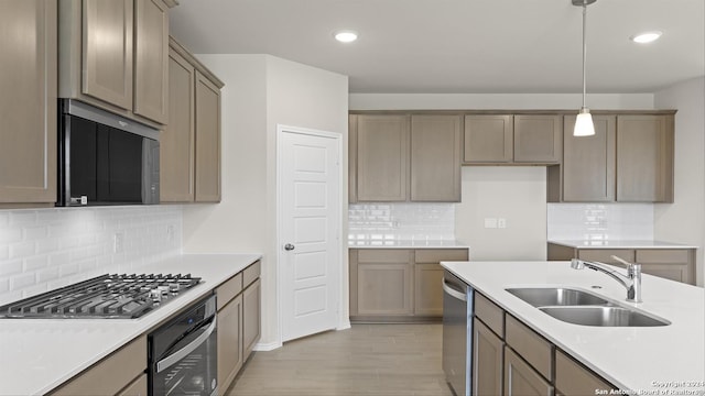 kitchen with appliances with stainless steel finishes, backsplash, sink, pendant lighting, and light hardwood / wood-style flooring