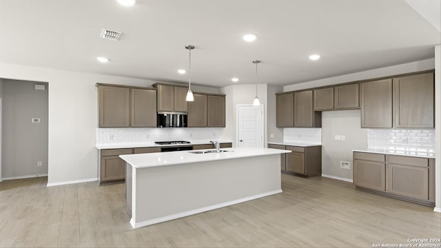 kitchen featuring sink, backsplash, decorative light fixtures, a center island with sink, and light wood-type flooring