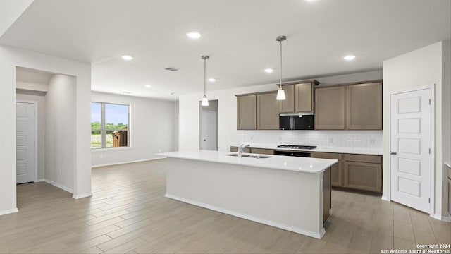 kitchen featuring decorative backsplash, a center island with sink, decorative light fixtures, and light hardwood / wood-style flooring