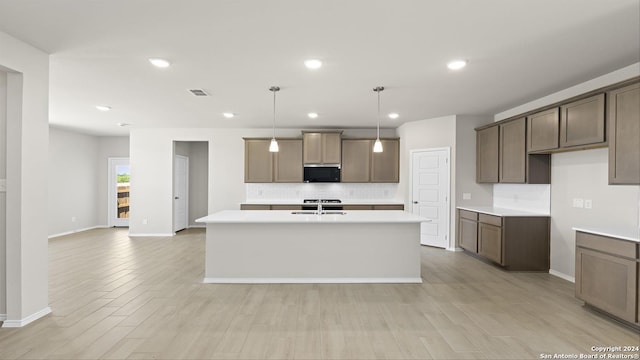 kitchen with pendant lighting, sink, light wood-type flooring, and a kitchen island with sink