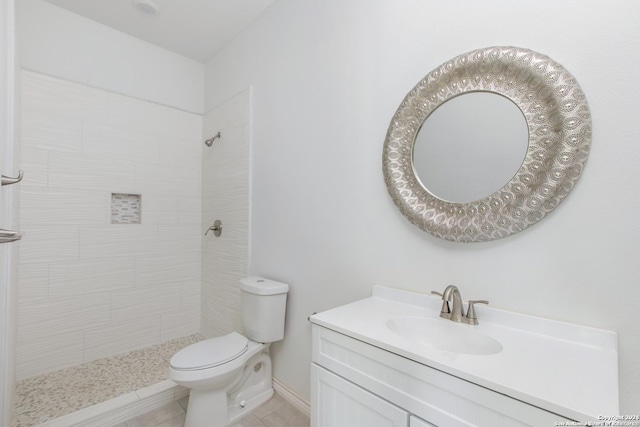 bathroom with tiled shower, tile patterned flooring, vanity, and toilet