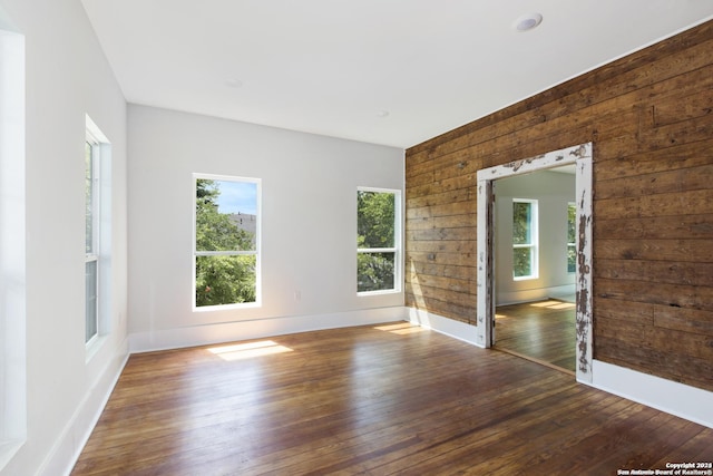 empty room with wood walls, dark hardwood / wood-style flooring, and a wealth of natural light