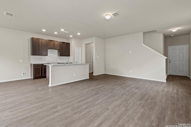 kitchen featuring tasteful backsplash, dark brown cabinetry, sink, hardwood / wood-style flooring, and an island with sink