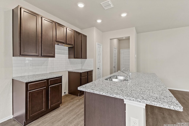 kitchen featuring a kitchen island with sink, sink, dark brown cabinets, and light wood-type flooring